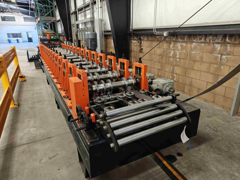 The roll forming feeder section, showing a set of motorized rollers or guides that push the material accurately into the entry guide of the main roll forming stands.