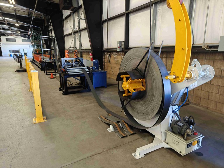 A large industrial uncoiler machine holding a massive roll of metal coil, designed to unwind the material smoothly into the production line.
