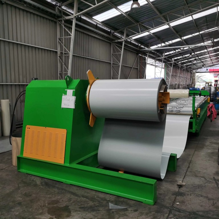 Una máquina desenrolladora motorizada de alto rendimiento que sostiene un rollo grande de bobina de acero galvanizado, lista para alimentar el metal en una línea de formación de rollos de láminas para techos de gran envergadura.
